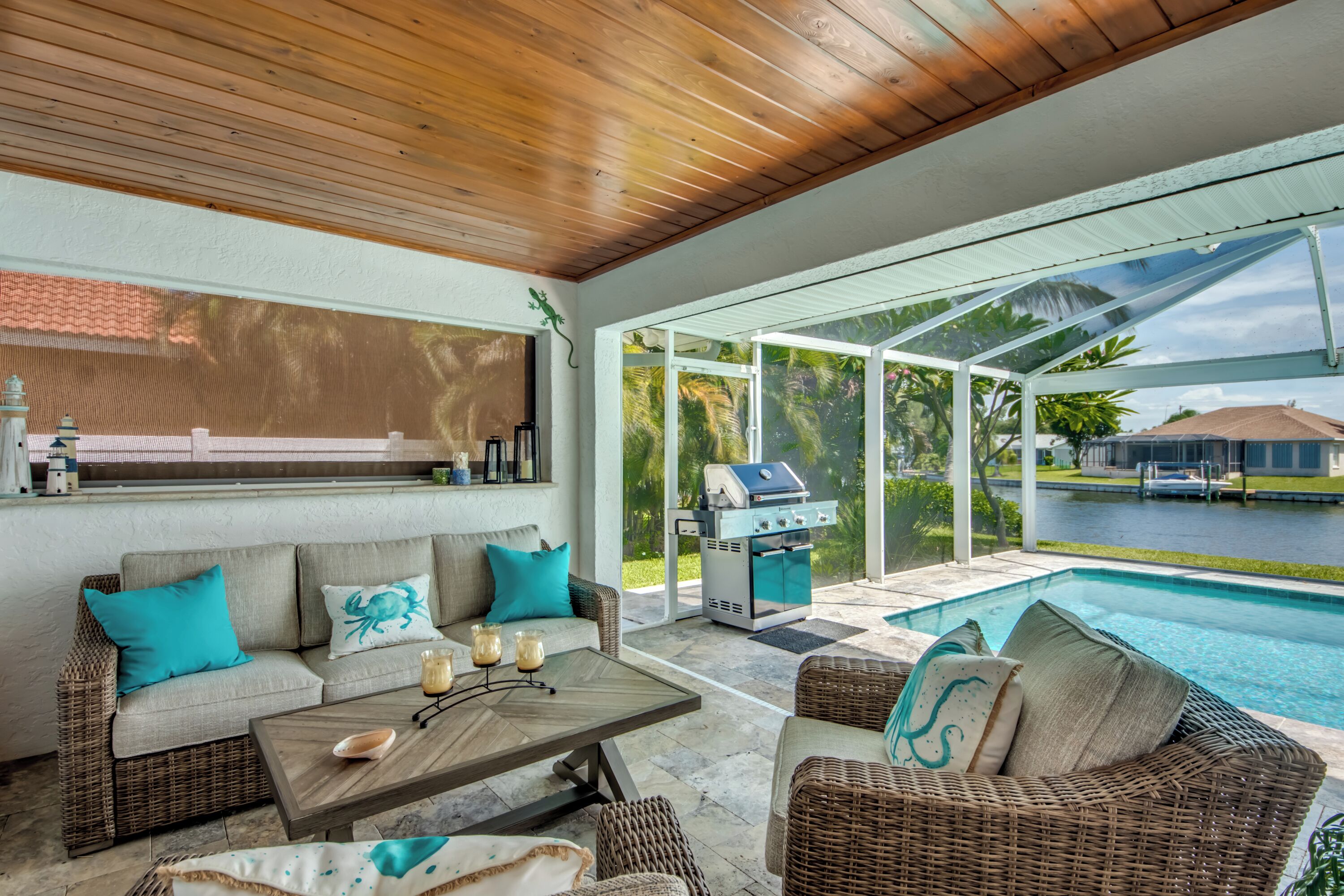 A covered outdoor seating area with a pool, wicker furniture, and a grill.