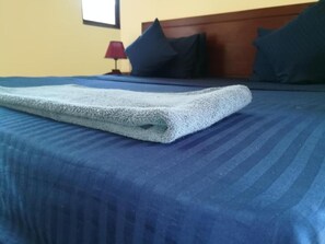 A neatly made bed with a blue bedspread and a folded white towel on top. - Lake Bliss (Dambulla)
