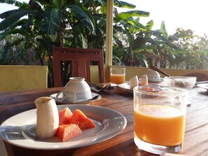 A wooden table with a plate of food, a glass of orange juice, and a cup. - Lake Bliss (Dambulla)