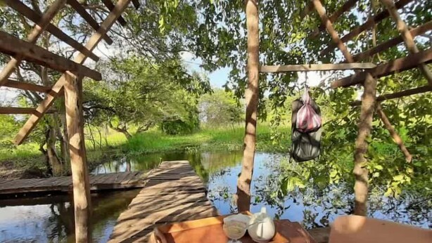 Une terrasse en bois surplombant l’eau, avec une table dressée pour deux personnes, comprenant des tasses et une théière.