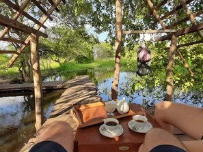 A wooden deck over water with a table set for two, including cups and a teapot. - Lake Bliss (Dambulla)