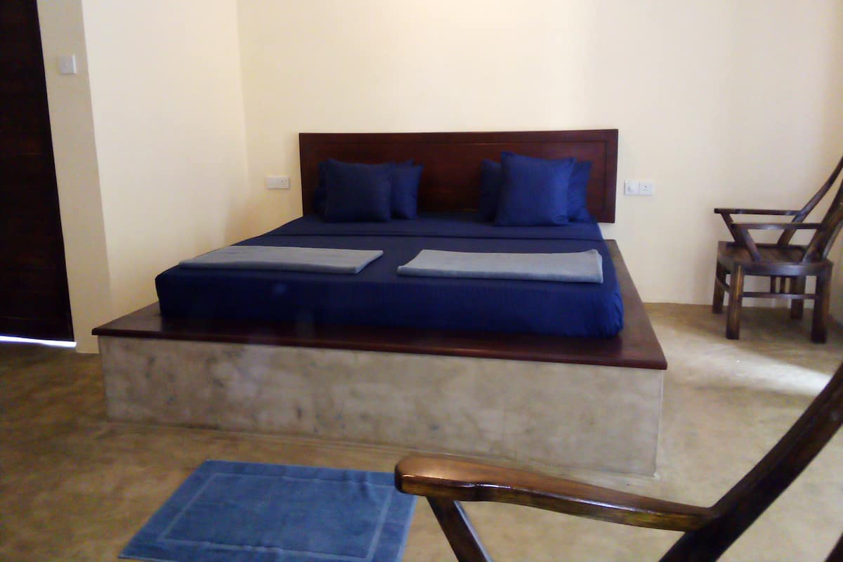 Un dormitorio con cama, almohadas, una silla y una alfombra pequeña.