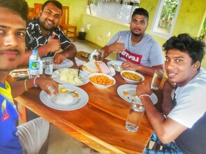 A group of people sitting around a wooden table with various dishes, including rice, curry, and bread. - Lake Bliss (Dambulla)