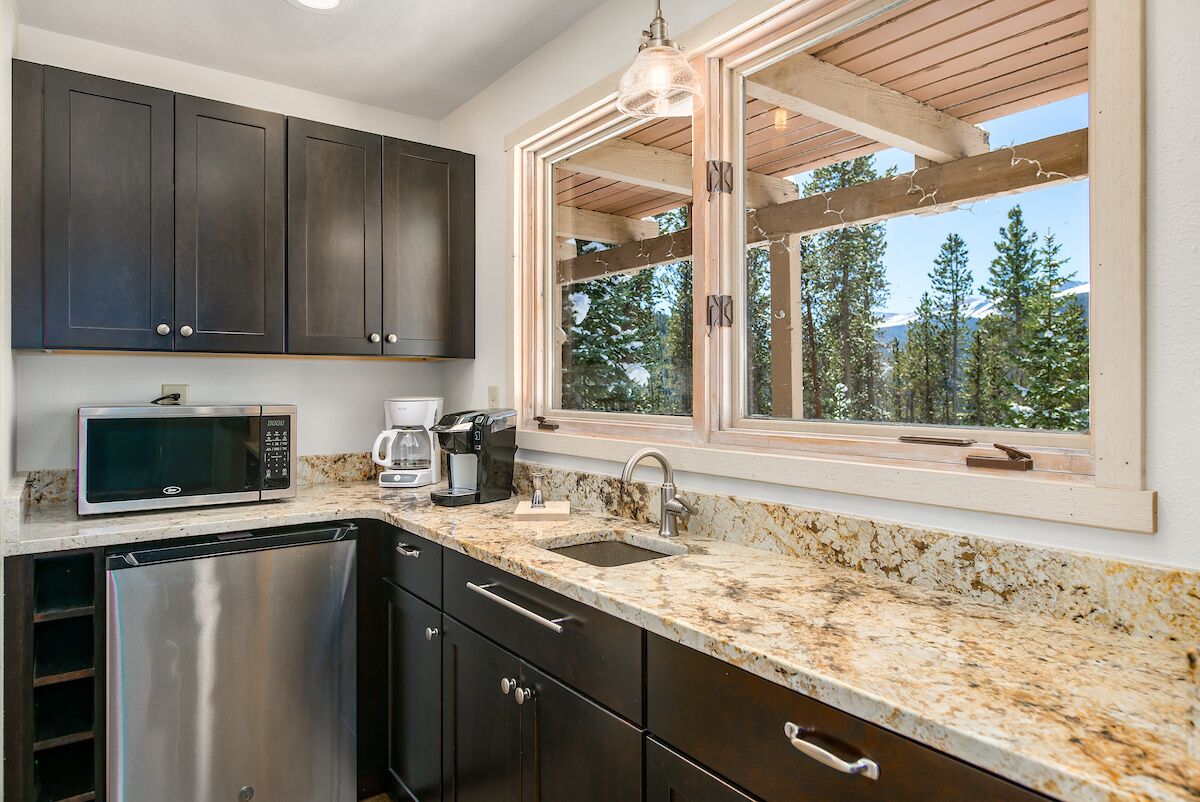 A kitchen with dark cabinets, a stainless steel dishwasher, a microwave, a coffee maker, and a sink.