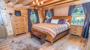 A cozy log cabin bedroom with a wooden bed, a bench, a dresser, and a television on a wooden cabinet. - Bear Creek Mining Lodge: Mountain Style, Hot Tub (Breckenridge)
