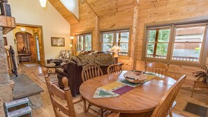 A cozy cabin interior with a wooden dining table, chairs, a fireplace, and large windows. - Bear Creek Mining Lodge: Mountain Style, Hot Tub (Breckenridge)