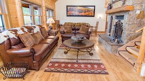 A cozy log cabin interior with a leather sofa, a fireplace, and a framed autumn landscape painting. - Bear Creek Mining Lodge: Mountain Style, Hot Tub (Breckenridge)