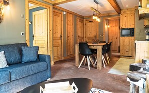 Un salon confortable avec un canapé bleu, un coin repas avec une table et des chaises en bois, et une cuisine dotée de meubles en bois et d’un four à micro-ondes.