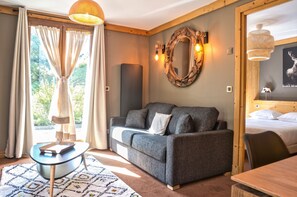 Una habitació acollidora amb un sofà gris, un mirall rodó, un llit amb roba blanca i un sostre de fusta.