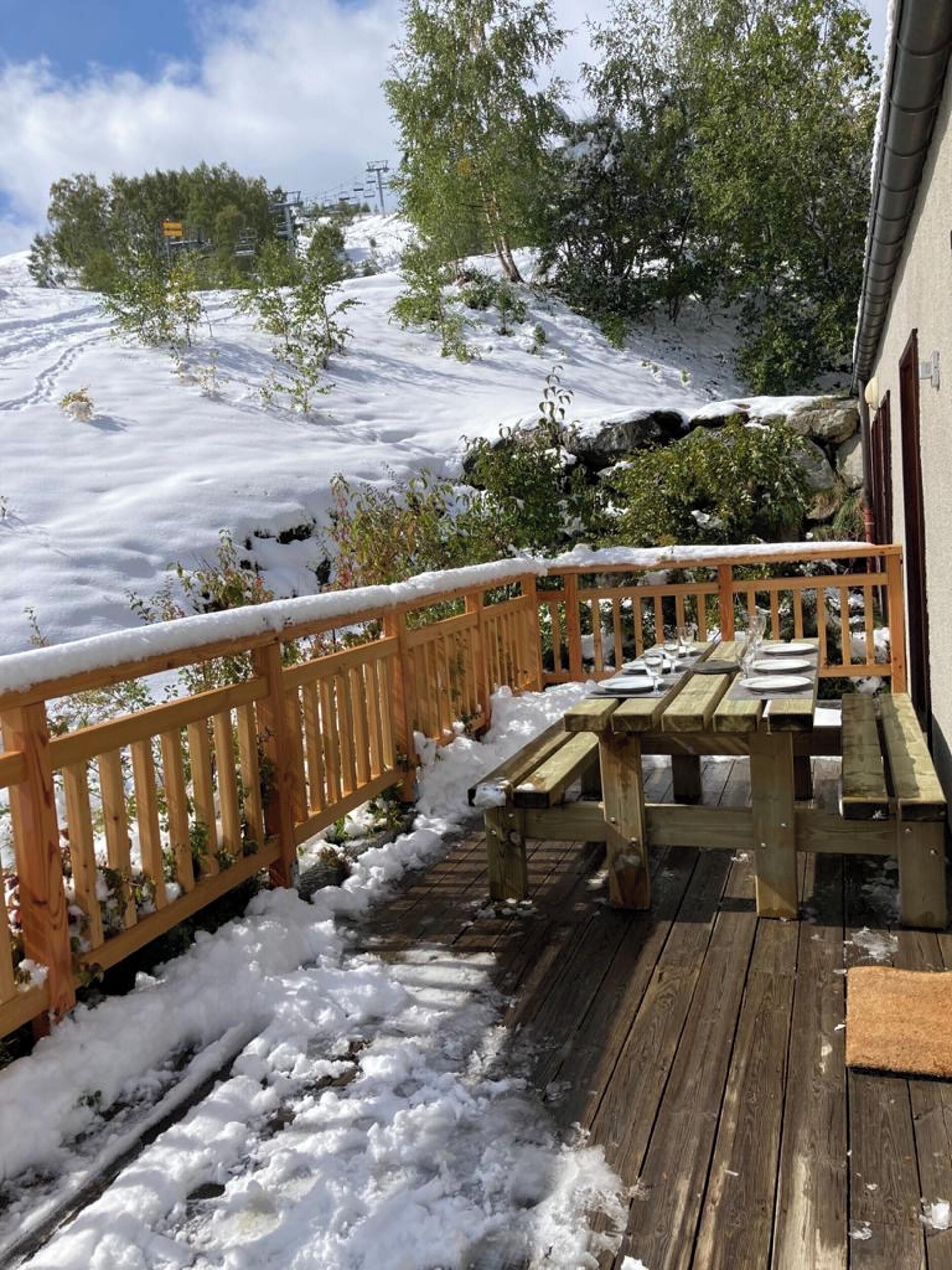 Une terrasse en bois avec une table de pique-nique et des bancs, entourée d’un paysage enneigé et d’arbres.