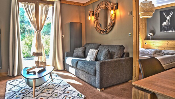 A cozy room with a sofa, a small table, a bed, and a large mirror on the wall. - Homerez - Apt. Mountain View - Les Deux Alpes (Les Deux Alpes)