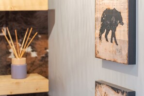 Un mur orné d’une œuvre d’art encadrée représentant la silhouette d’une vache, une étagère en bois avec un chandelier, et un arrière-plan flou.