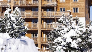 A multi-story wooden building with balconies, surrounded by snow-covered trees. - Homerez - Apt. Mountain View - Les Deux Alpes (Les Deux Alpes)