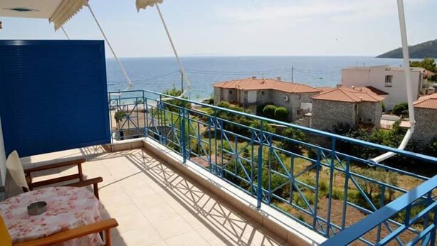Un balcón con vista al mar, una mesa con sillas y una barandilla azul.