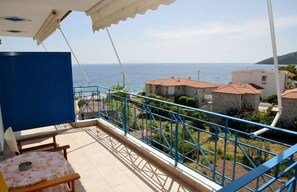 Uma varanda com vista para o mar, uma mesa com cadeiras e um corrimão azul.