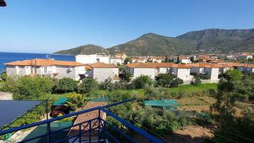 A balcony with a view of a coastal town, stone buildings, and a mountain in the background.