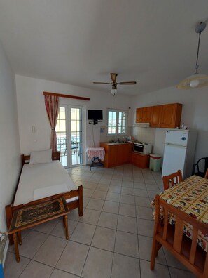 Un espacio habitable compacto con cama, mesa de comedor, zona de cocina con refrigerador y ventilador de techo.
