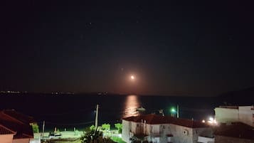 Une ville côtière de nuit, avec une lune visible, des bâtiments aux toits rouges et une étendue d’eau.