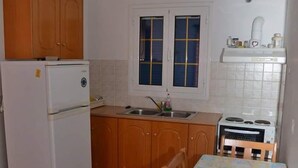 Una cocina compacta con armarios de madera, un refrigerador blanco, una estufa, un lavamanos y una mesa con sillas.