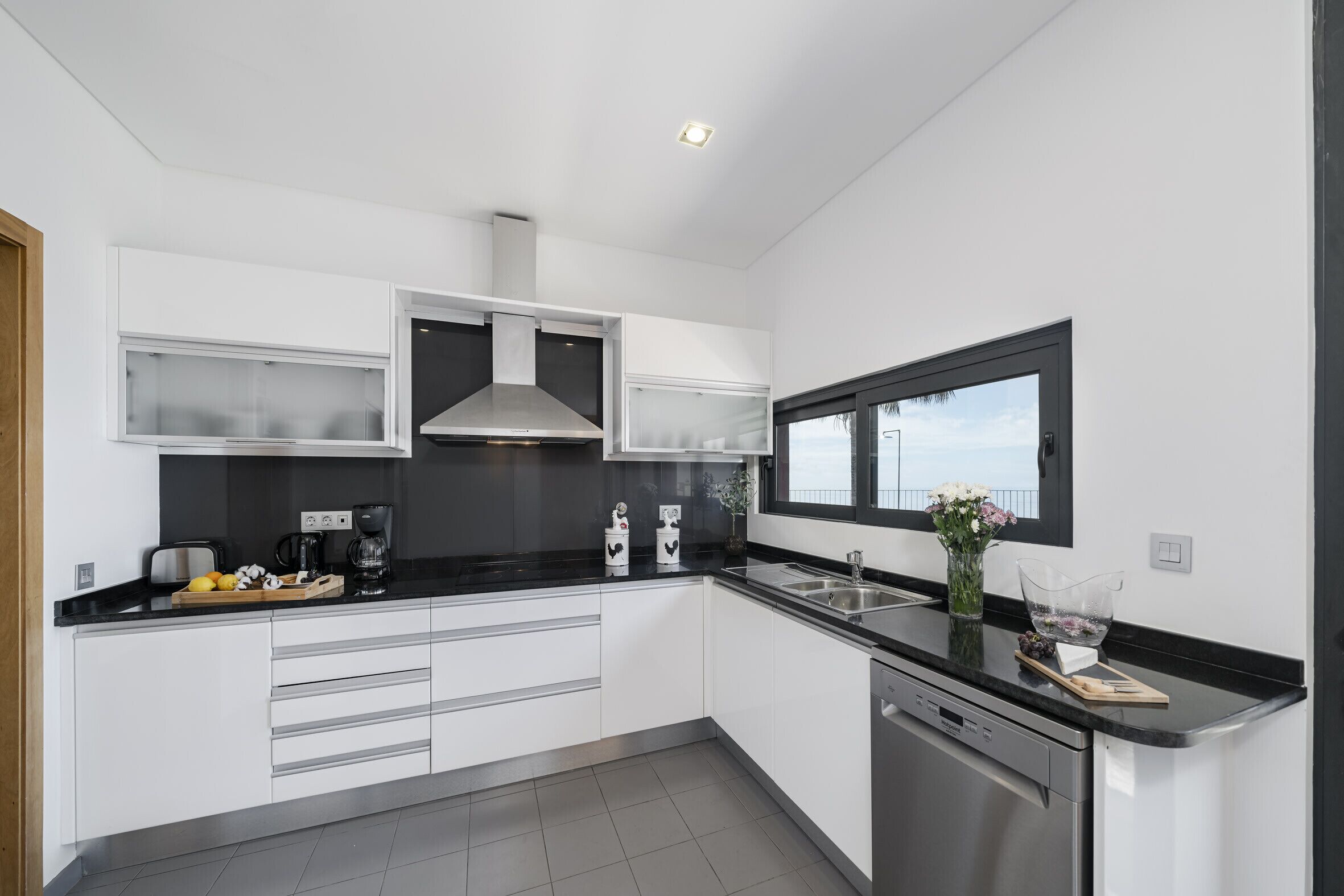 A modern kitchen with white cabinets, a black countertop, stainless steel appliances, and a window.