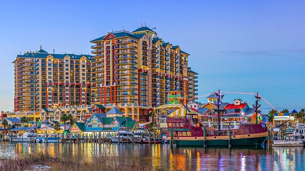 Un hotel frente al mar con varios balcones, un puerto deportivo con barcos y una variedad de edificios coloridos a lo largo de la costa.