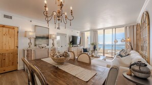 Amplia sala de estar con una mesa de comedor de madera, un candelabro y un gran ventanal con vistas al mar.