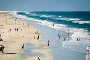 A beach with people walking and swimming.