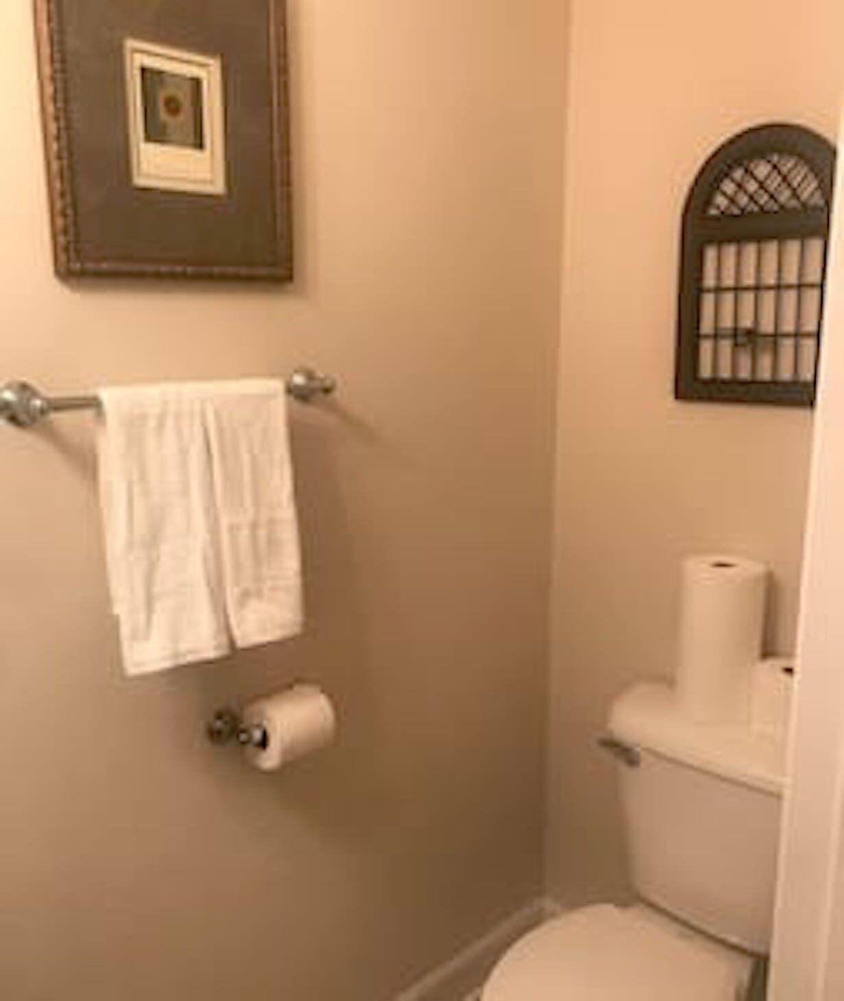 A small bathroom with a toilet, a towel rack with two towels, and a toilet paper holder.