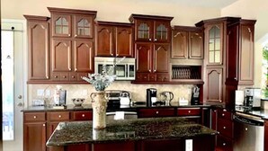 A kitchen with dark wooden cabinets, a granite countertop, and stainless steel appliances. - South Hampton 75” TV Golf Club Saint Augustine Golf Course View! (St. Augustine)