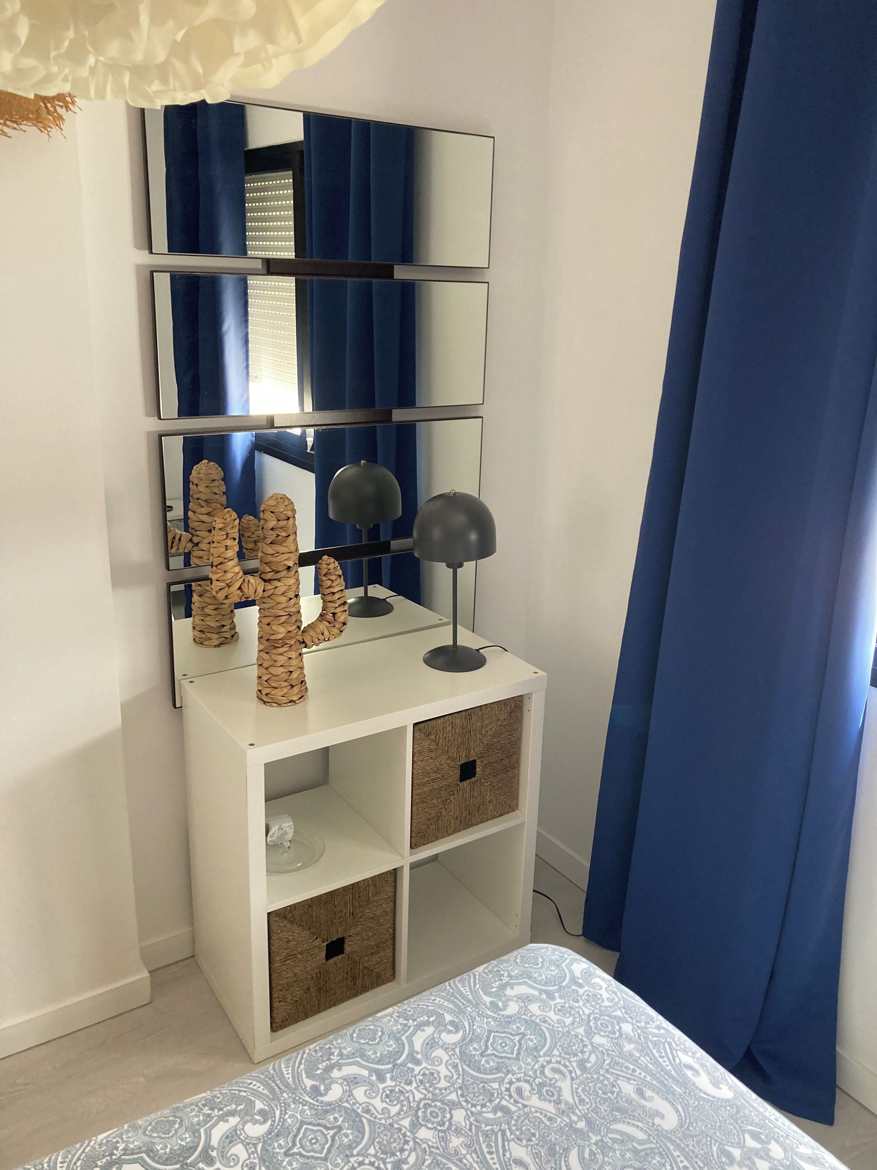 Un dormitorio con cama, una mesita de noche con lámpara, un espejo y cajas de almacenamiento.