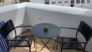 Un balcon avec deux chaises en métal noir et une petite table ronde, donnant sur un paysage urbain avec des bâtiments blancs et une rue.