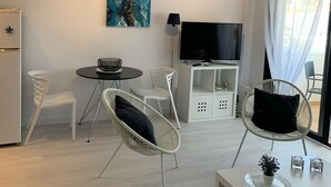 Un salon moderne avec un canapé blanc, une table ronde, un téléviseur et un tableau accroché au mur.