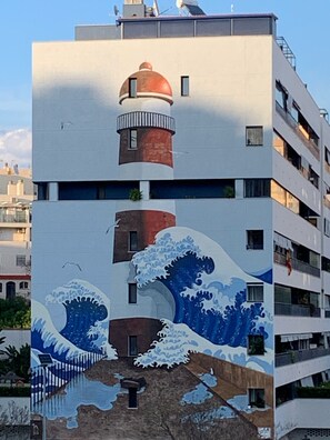 A multi-story building with a wave painting on the facade, a red and white tower, and balconies. - Apartment sea view, bright, cozy, facing the port, swimming pool, parking, wifi. (Estepona)