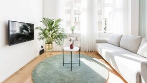 A modern living room with a flat-screen TV, a round table with a vase of flowers, a potted plant, and a white sofa. - Comfortable Studio in the Center | Close to the Park and the Fair (Poznan)