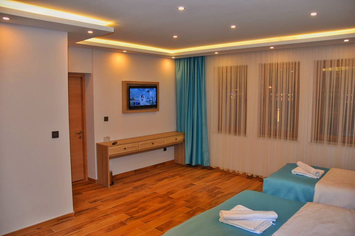 Habitación de hotel con suelo de madera, televisor montado en la pared, un banco y dos camas con toallas.