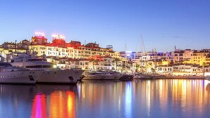 Un hotel frente al agua con varias embarcaciones amarradas, un puerto deportivo y un paisaje urbano con edificios al fondo.