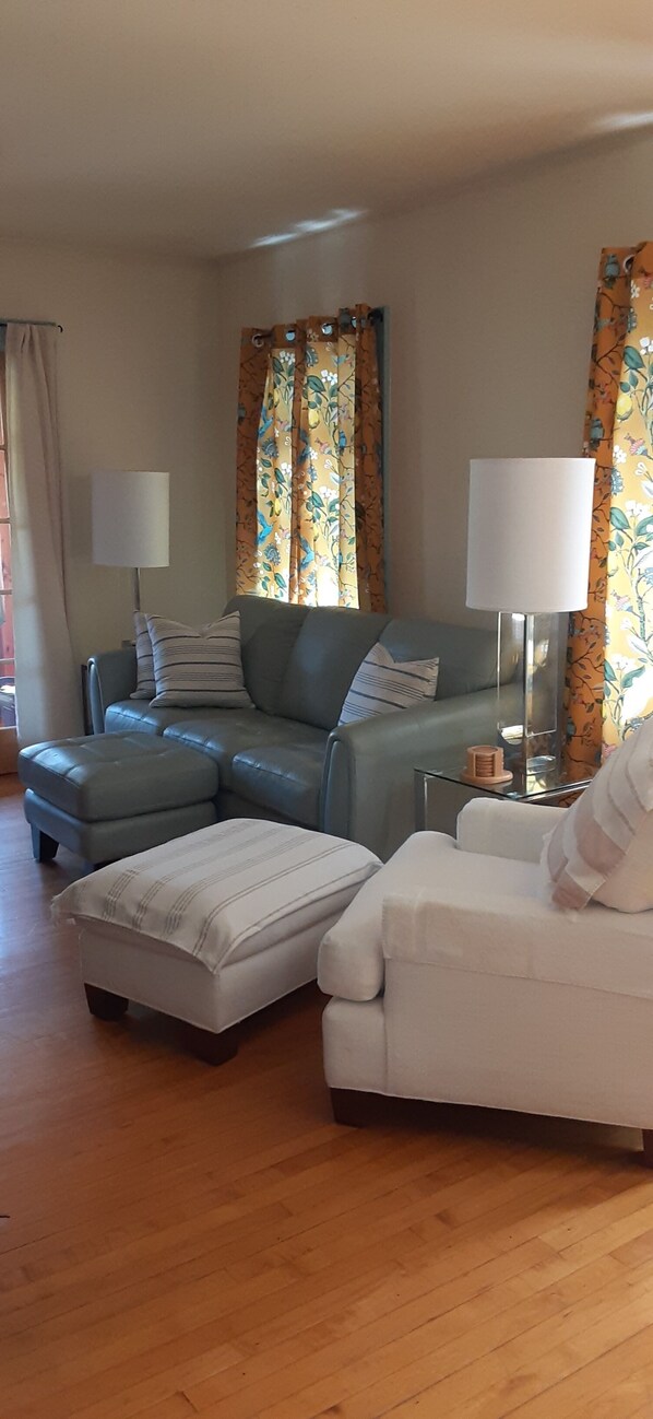 A living room with a sofa, ottoman, and armchair, a lamp, and curtains.