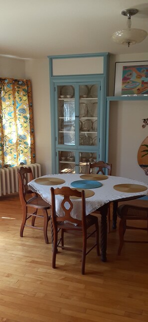 A dining area with a table set for four, surrounded by wooden chairs, a blue cabinet with glass doors, and a radiator.