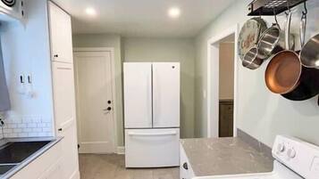 A kitchen with white cabinets, a double-door refrigerator, a stove with black burners, and hanging pots.