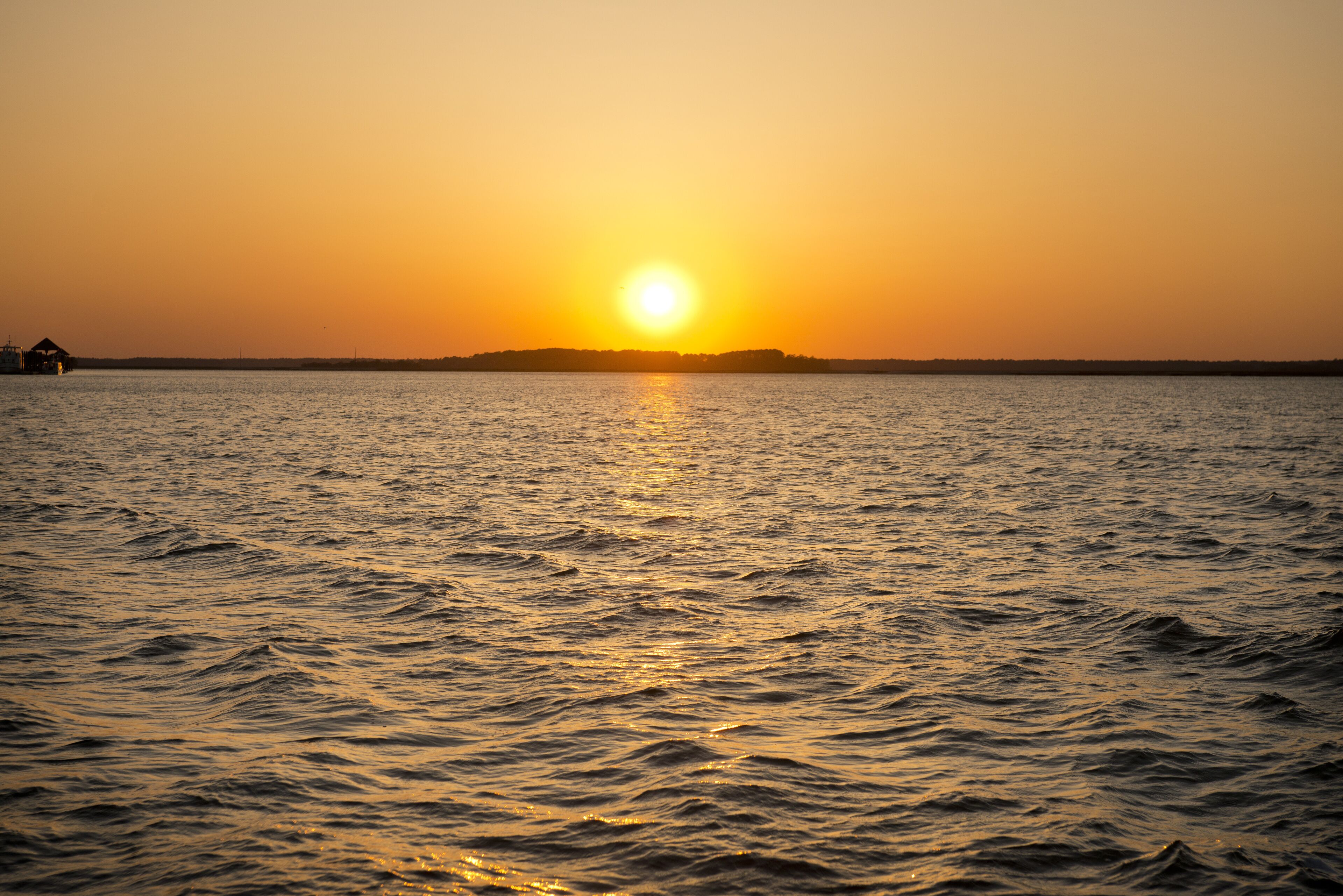 A sunset over a calm body of water with a distant shoreline.