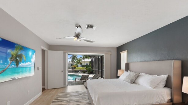 Ein Schlafzimmer mit Bett, Deckenventilator, Blick auf einen Pool und einer Tür zu einem Außenbereich.