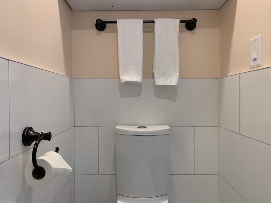 A bathroom with a toilet, a towel rack with two towels, and a toilet paper holder.