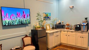 A modern kitchen with white cabinets, a built-in microwave, a refrigerator, and a coffee machine. There is a TV mounted on the wall displaying a flower scene. - The Cabot Lodge (Beverly)