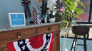 A wooden desk with a red, white, and blue decorative cloth, a sign with contact information, and a potted plant. - The Cabot Lodge (Beverly)