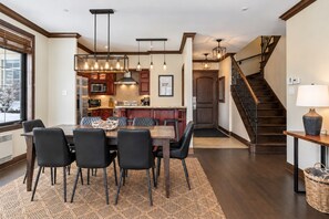 A modern kitchen with a dining area, featuring a wooden table, chairs, and pendant lighting.