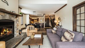 A spacious living room with a fireplace, a sofa, a coffee table, and a dining area in the background.