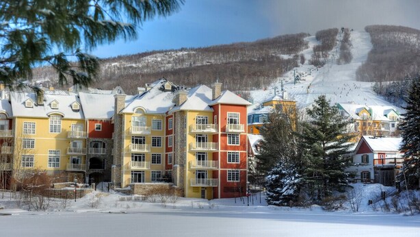 A multi-story hotel with balconies and a ski slope in the background.