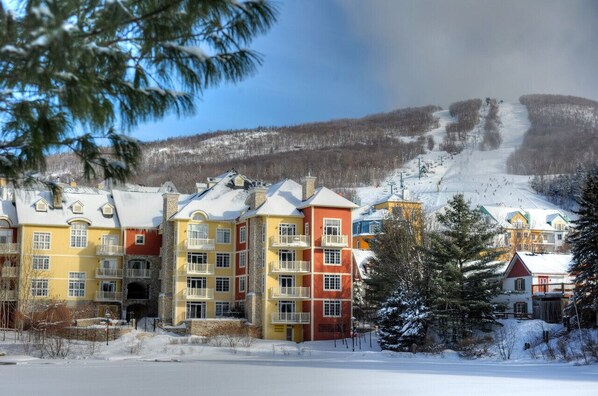 Ein mehrstöckiges Hotel mit Balkonen und einer Skipiste im Hintergrund.