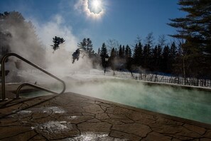 Ein geothermales Spa mit einem Steinebecken, aufsteigendem Dampf und blauem Himmel.
