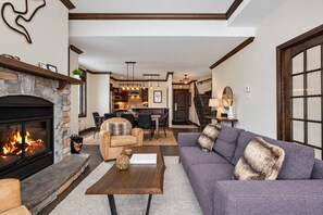 A living room with a fireplace, a sofa, a coffee table, and a dining area in the background.